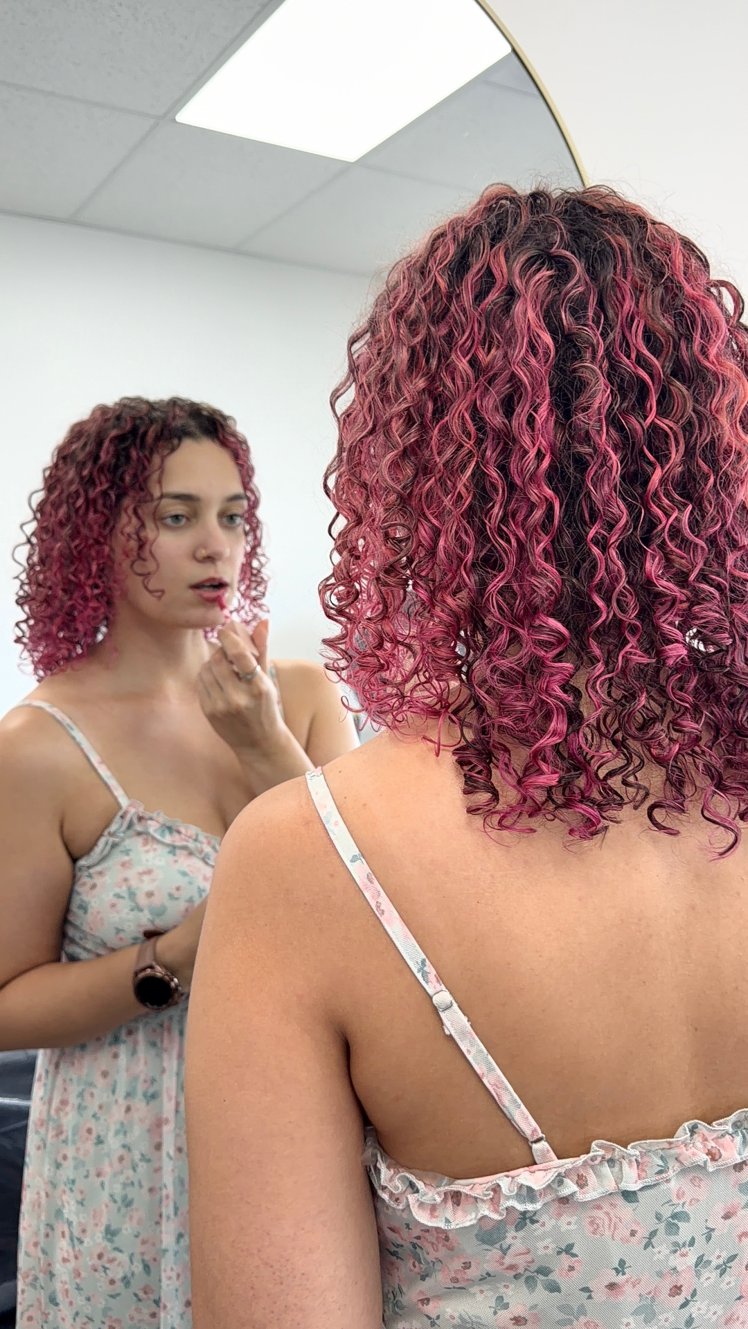 Client with vivid pink and burgundy defined spiral curls reflected in a salon mirror