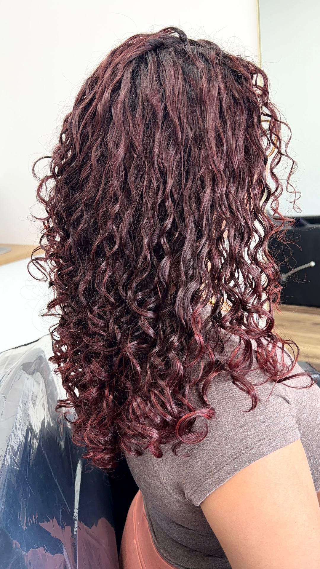 Client with long burgundy curls styled with glossy definition